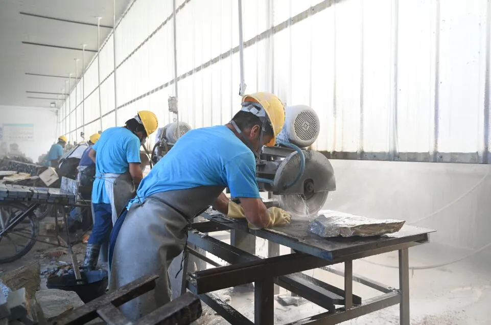 Worker cutting stacked stone panels in a workshop.